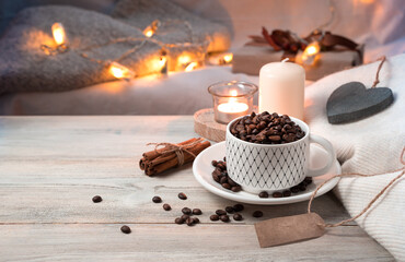 A Cup of coffee full of coffee beans on a cozy evening holiday background with lights. Side view with space for copying. Concept of holiday backgrounds.