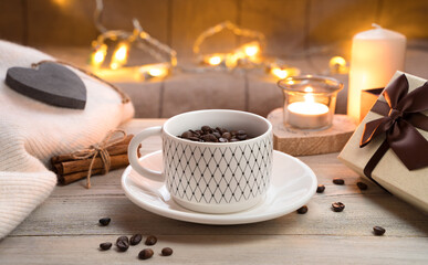 A Cup on a saucer, not fully filled with coffee beans on a wooden background with burning lights in the background. Side view. Concept of coffee holiday backgrounds.