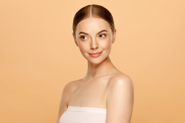 Portrait of young beautiful woman wearing towel around body after shower, looking away, isolated on brown background