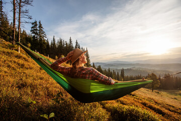 Woman hiker resting after climbing in a hammock at sunset - 391109695