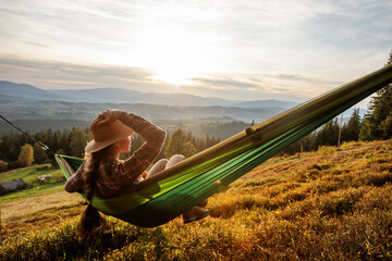 Woman hiker resting after climbing in a hammock at sunset - obrazy, fototapety, plakaty