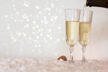 Pouring champagne from bottle into glass on snow with bokeh background with copy space