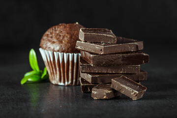 Chocolate cupcake with icing and chocolate bar in Dark lighting,Homemade delicious chocolate muffin on wooden background close-up