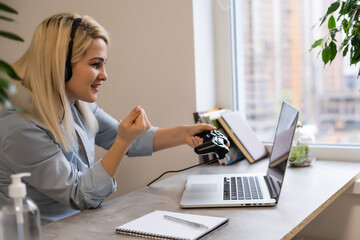 young successful business woman in the office with headphones and with a joystick playing computer...