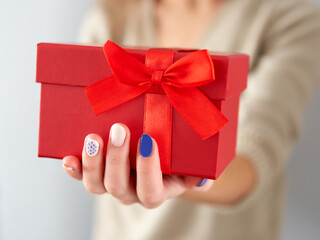 Female hand hold a red gift box. Birthday and Christmas gift with a red bow and ribbon. Giving a gift in a box. Time for gifts and Christmas.