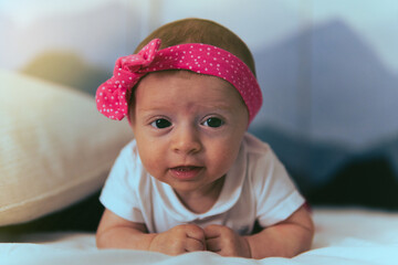 A baby lying in bed with a pink headband.