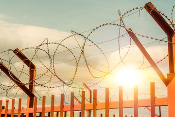 Red fence with barbed wire on the background of the sky with clouds sunset. Restricted area, prison...