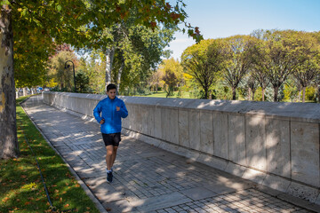man jogging in the city in autumn. he wears a blue coat and shorts. autumn colors in the city.