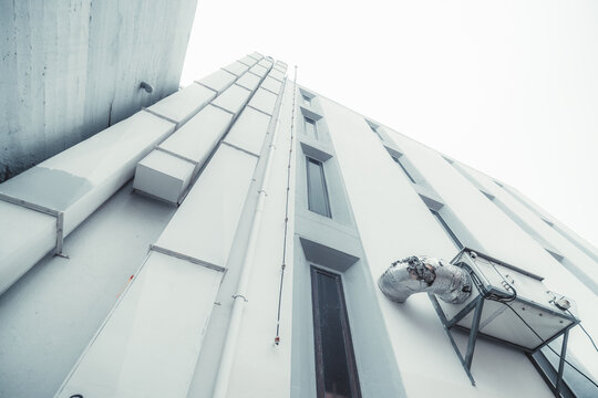 Wide-angle bottom view of a white building facade with three vertical ventilation ducts, tube, and a lightning rod on the left, a group of elongated windows and an external module of air conditioner