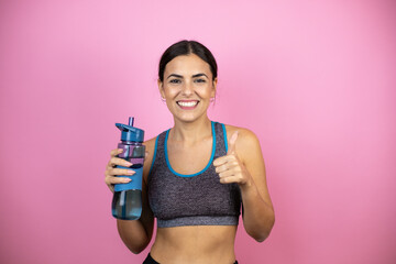 Young beautiful woman wearing sportswear over isolated pink background pointing thumb up to the side smiling happy