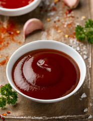Barbecue sauce in white bowl on wooden board with herbs