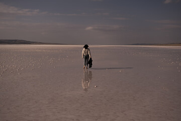 woman walking on the salt lake with her jacket in hand. woman's reflection on shallow water. the concept of peace, quiet, loneliness and rest. the woman is wearing a lace patterned shirt.