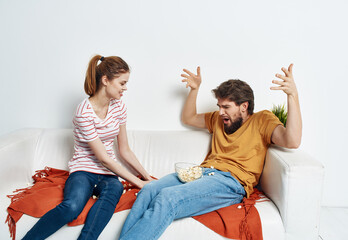 Fun man and energetic woman watching TV on the couch popcorn in a plate family communication