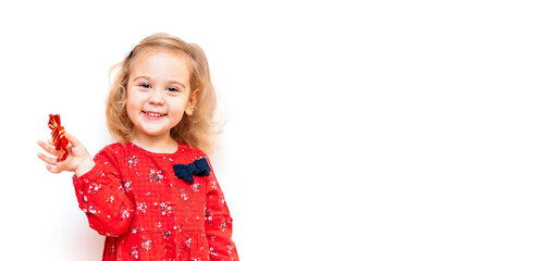 Smiling happy little girl in red dress on white background holding candy in hand