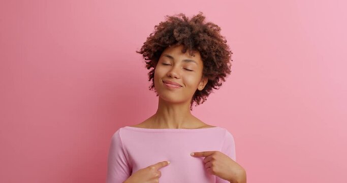 This is me. Self confident serious woman in casual clothing points at herself being proud of own achievements poses against pink background. Assertive boastful lady brags her accomplishments
