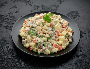 Olivier salad, traditional Russian food in black plate on black rustic table