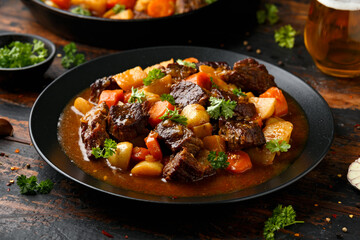 Beef Stew with carrot and baby potato in black plate on wooden table