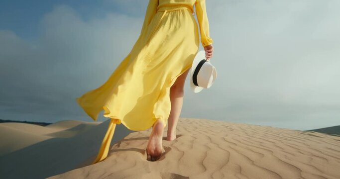 Back view of woman in beautiful dress flattering on wind. Cinematic modern yellow fabric waving on cloudy blue sky background. Fashion dress slow motion. Commercial footage for clothing business 4K