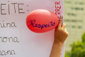 Pessoa segurando cartaz com um balão vermelho escrito RESPEITO. Imagem feita durante uma...