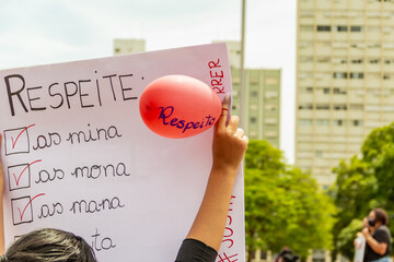 Pessoa segurando cartaz com um balão vermelho escrito RESPEITO. Imagem feita durante uma...