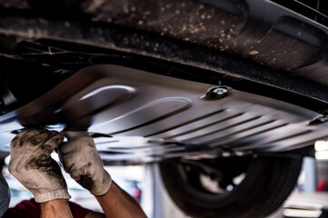 Fototapeta Mechanic installs underbody protection on a raised car obraz