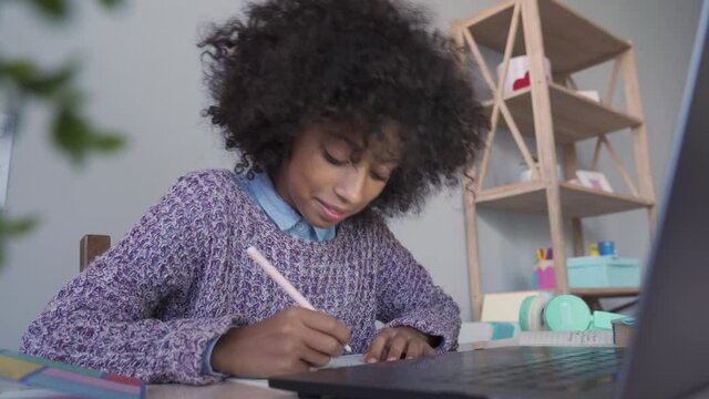Happy cute kid girl video calling learning in virtual school on laptop at home. Smart african child talking with remote web teacher on distance conference computer class. Children learning at home.
