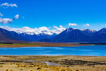 Snow covered mountains and green valleys with a lake in New Zealand