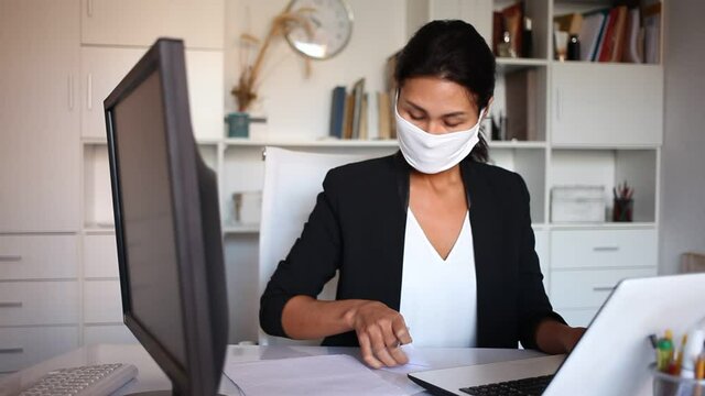 Professional business woman in protective medical mask using laptop at workplace in office 