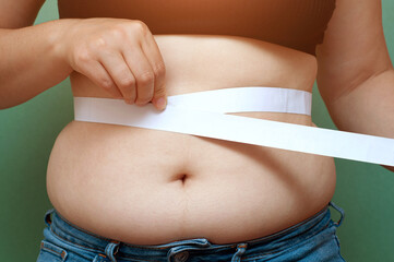 Overweight fat woman measuring her belly fat with measuring tape