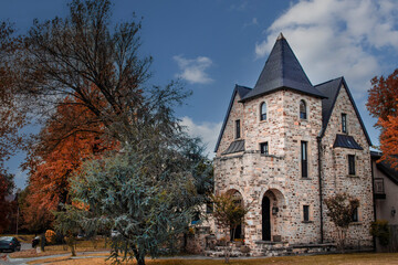 Fototapeta premium Three story rock house with tower in Autumn with pretty foliage and trees parked along the road