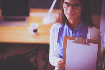 Young woman standing near desk with laptop holding folder