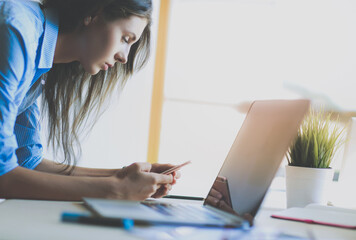 Young woman standing near desk with instruments, plan and laptop