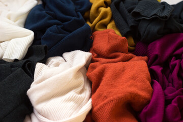 Lots of knitted sweaters scattered around. Bright multi-colored womens sweaters lie in a mess,...
