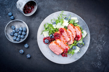 Modern style gourmet duck breast filet with rocket salad and cranberry relish offered as close-up on a design plate with copy space