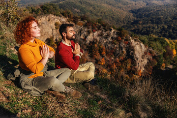 Naklejka na ściany i meble Young couple enjoying nature on a beautiful sunny autumn day. Couple is sitting in lotus position and meditating on sun.
