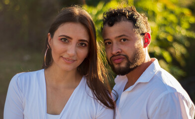 Fototapeta premium A romantic and lovely latin couple dressed in white with the ruins of a stone bridge behind and a beautiful sunset in the background