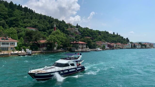 Footage of a luxury yacht passing and luxury houses in upscale neighborhood called "Kandilli" by Bosphorus in Istanbul. It is a beautiful summer scene on cloudy summer day. Camera moves forward.