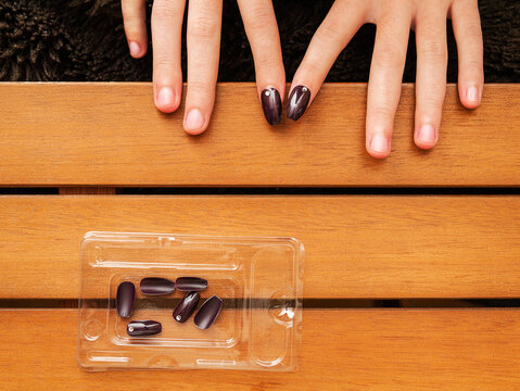 Female attaching fake nails on a wooden table, Cosmetic glamor procedure. Top down view. Spare nails in a plastic container
