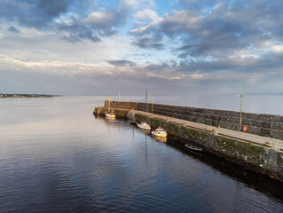 Obraz premium Small yachts and boat in Spiddal pier, county Galway, Ireland. Blue cloudy sky reflects in water. Warm sunny day. Nobody.