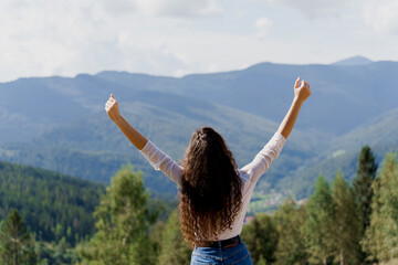 Tourism travelling in Ukraine. Girl girl raised her hands up and enjoys the mountain hills view. Feeling freedom in Karpathian mountains.