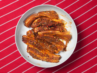 Raw pork belly slices in Korean style marinade on a white plate on a red and white table cloth. Meat industry product