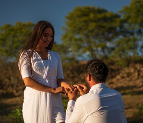 Marriage proposal of a latin couple dressed in white in a beautiful rural place with some stone walls and sunset in the background