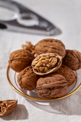 A group of walnuts laying on a glassware dish with a nutcracker in the background on a white table tablecloth