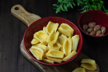 Buah Nangka or Jackfruit, one of tropical fruits popular in Indonesia. Cut into  half on red bowl and the seeds at behind. Dark wooden background. 