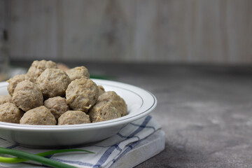 Bakso Sapi or Meatball traditional popular street food in Indonesia, served with clear soup, and noodles. Grey wooden background. Selective focus, copy space. 
