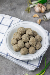 Bakso Sapi or Meatball traditional popular street food in Indonesia, served with clear soup, and noodles. Grey wooden background. Selective focus, copy space. 