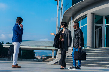 Two business colleagues discussing some reports outdoors while their young suited male colleague is talking on the phone