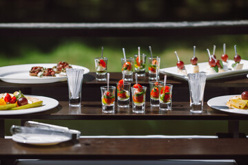 Cold appetizer at a wedding banquet, cherry tomatoes with mozzarella cheese and pesto in a glass. Canape selection on platter on banquet table.