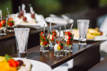 Cold appetizer at a wedding banquet, cherry tomatoes with mozzarella cheese and pesto in a glass. Cutlery and banquet table decoration.