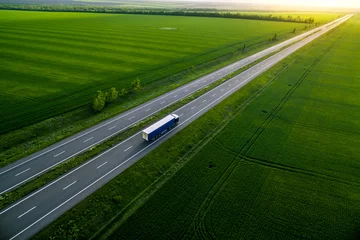 Fotobehang Weide blue truck driving on asphalt road along the green fields. seen from the air. Aerial view landscape. drone photography.  cargo delivery